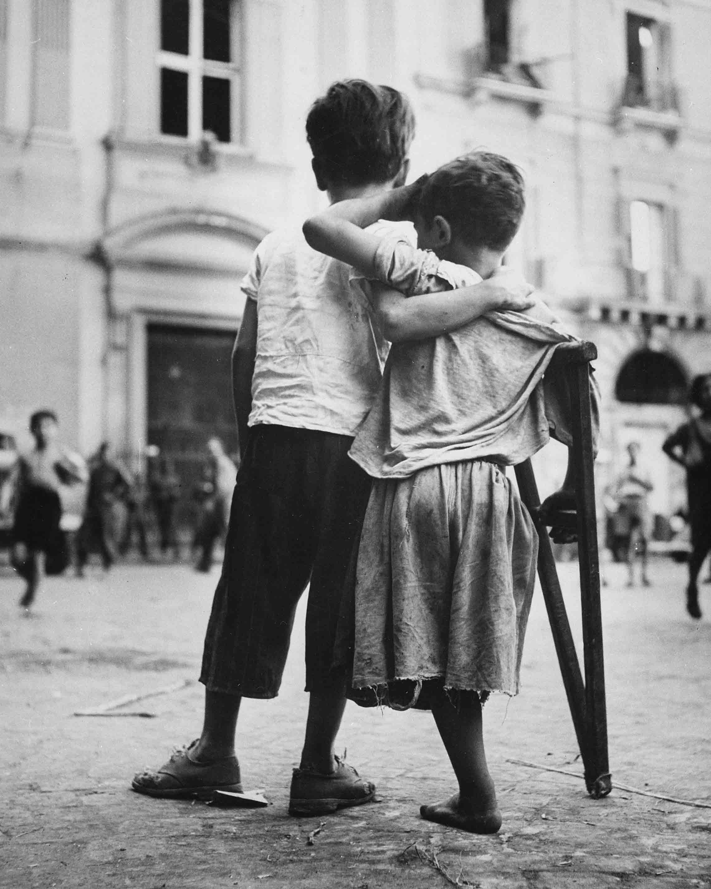 Bambini a Napoli, Italia. Un ragazzino aiuta il compagno con una gamba sola ad attraversare la strada, agosto 1944 Napoli, Italia. Autore sconosciuto o non fornito © courtesy U.S. Navy / U.S. National Archives and Records Administration